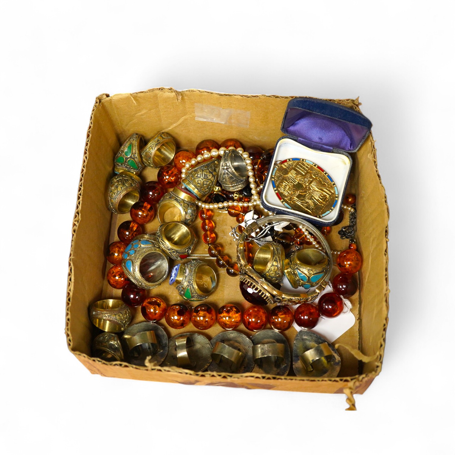 A collection of costume jewels, comprising: an Egyptian-style oval medallion pendant bordered in enamel; two imitation amber necklaces; a simulant pearl necklace; a pair of floral drop earrings; five lapis rings; a bangl